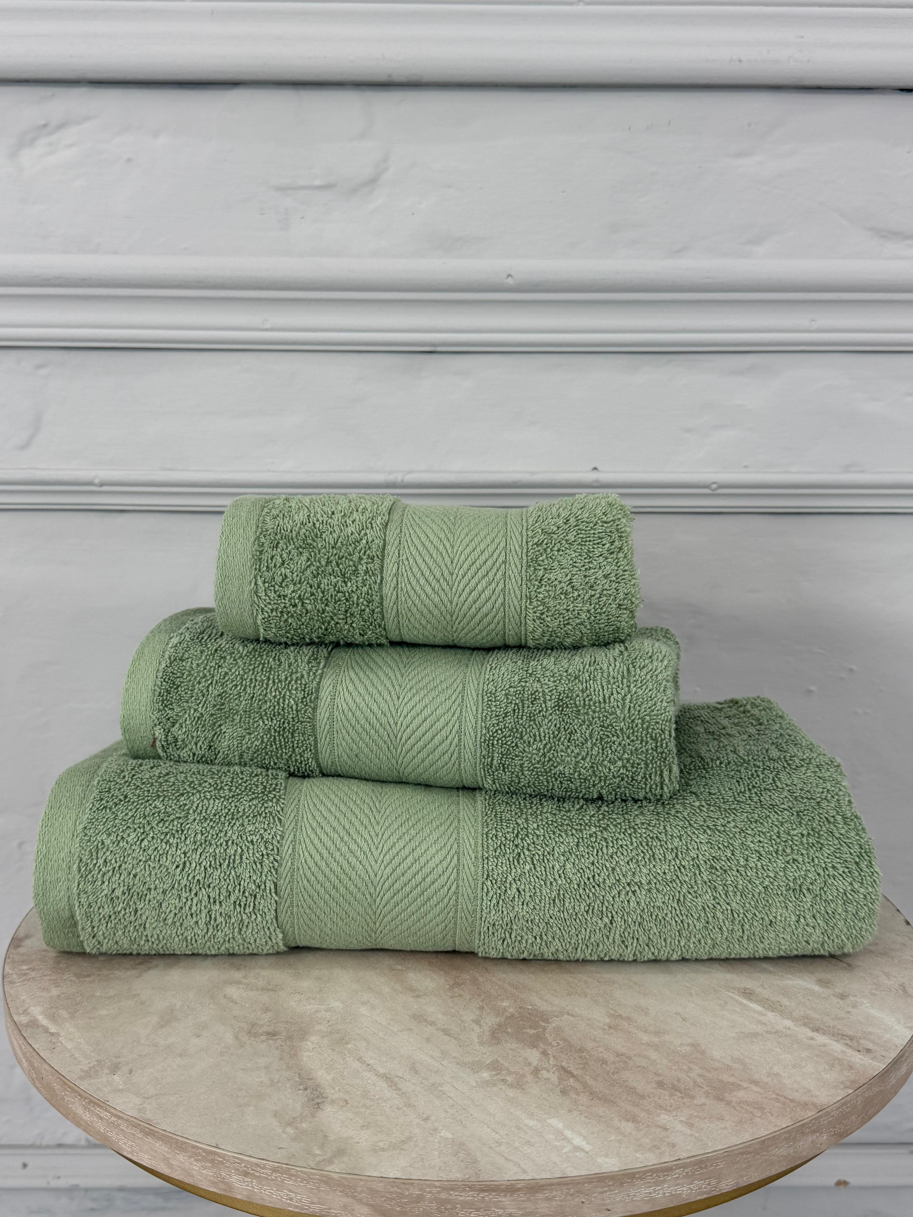 Set of three green towels stacked on a wooden surface with a gray wall background