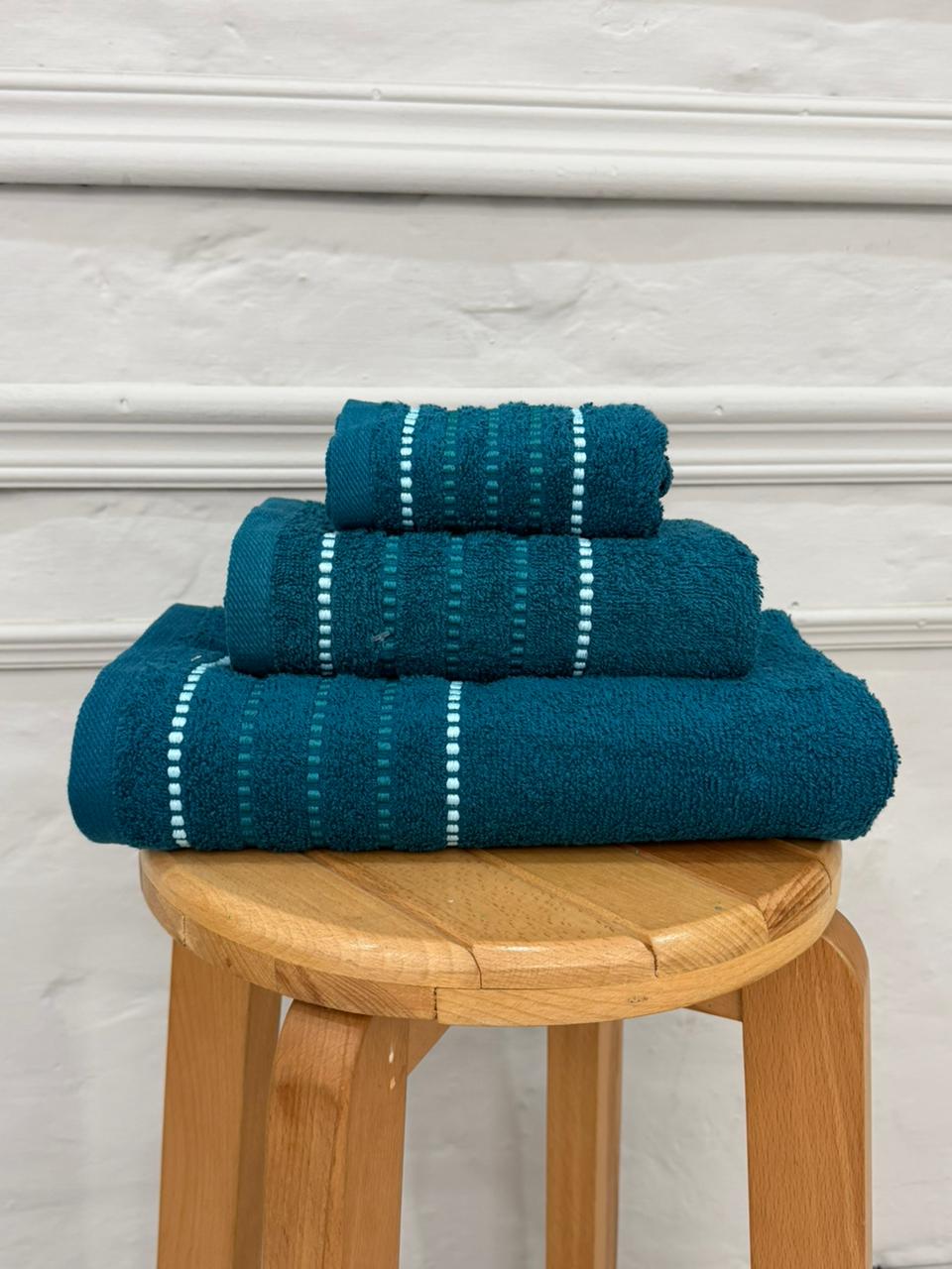 Set of three blue towels stacked on a wooden stool against a white wall.