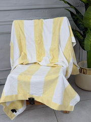 Yellow and white striped towel draped over a chair with a plant in the background