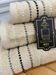 Three beige towels with black and gray stripes and a visible brand tag on a wooden surface.