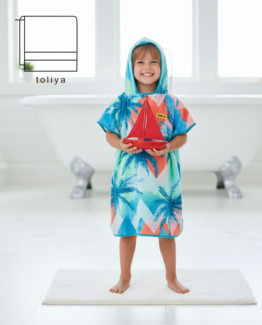 Child wearing a colorful hooded towel with palm tree and sailboat design, standing on a white platform.