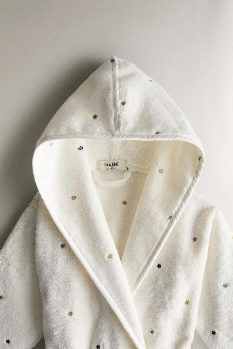 Child wearing a white hooded robe with small patterns on a white background