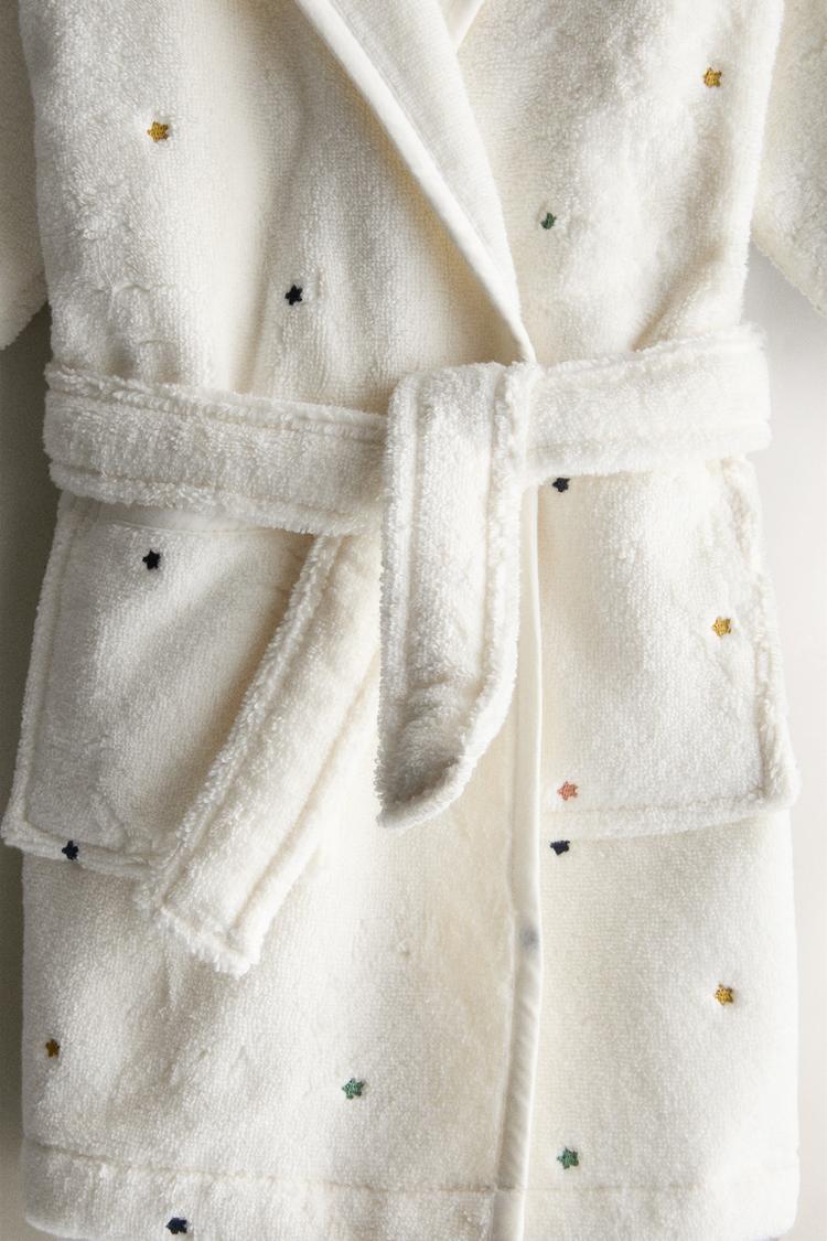 Child wearing a white hooded robe with small patterns on a white background