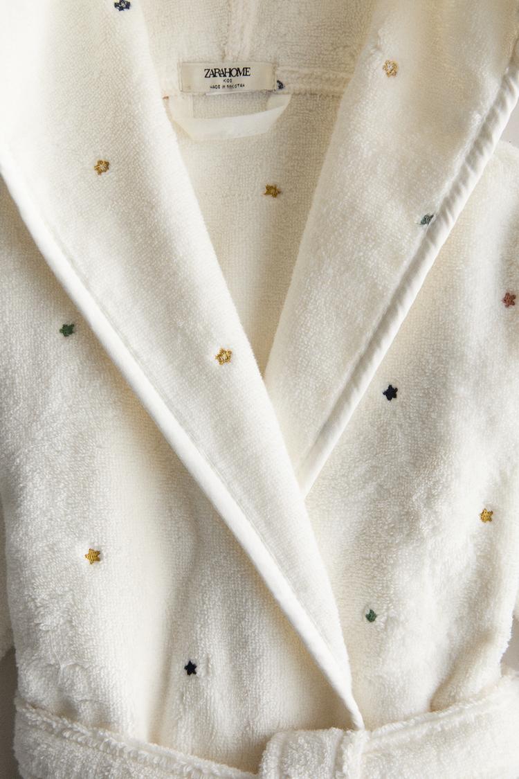 Child wearing a white hooded robe with small patterns on a white background