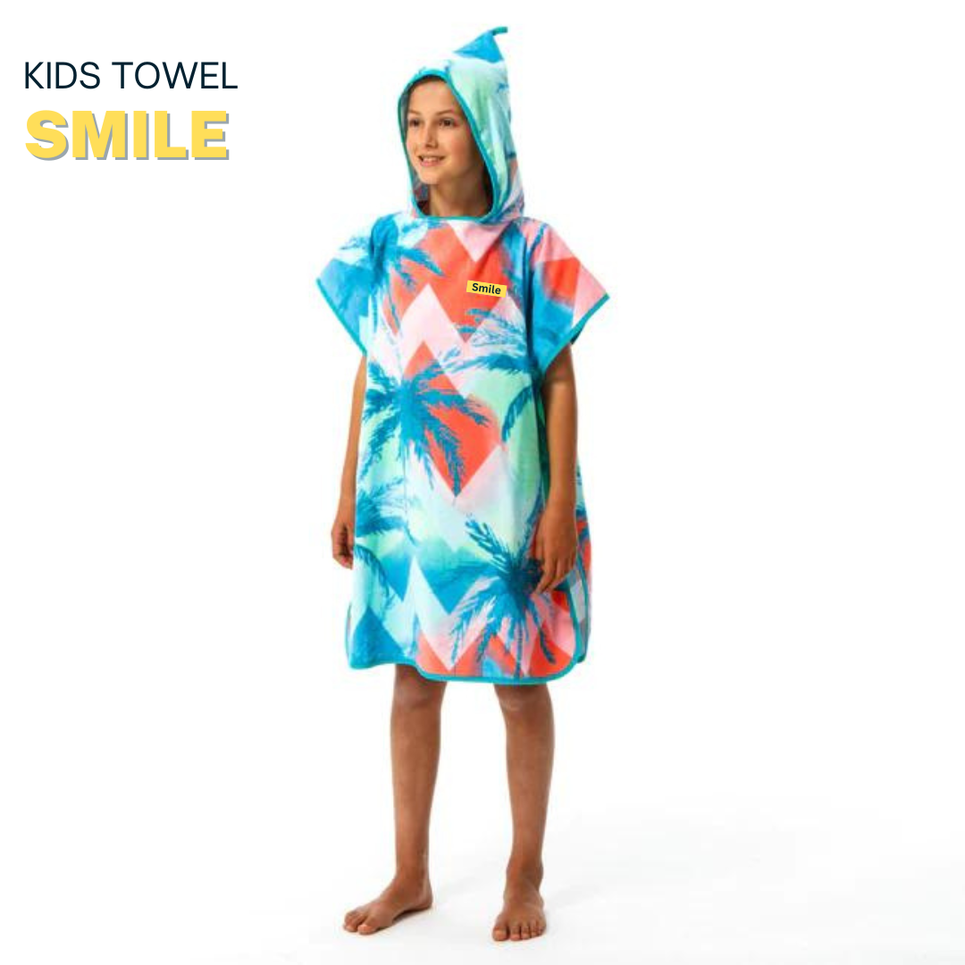 Child wearing a colorful hooded towel with palm tree and sailboat design, standing on a white platform.