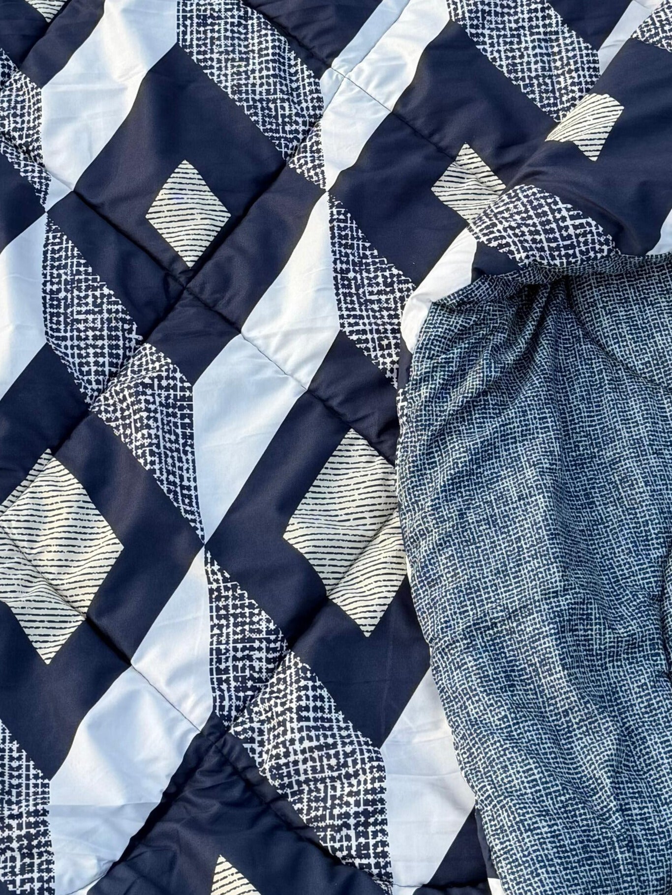 Close-up of a quilt with blue and white geometric pattern and a piece of fabric.
