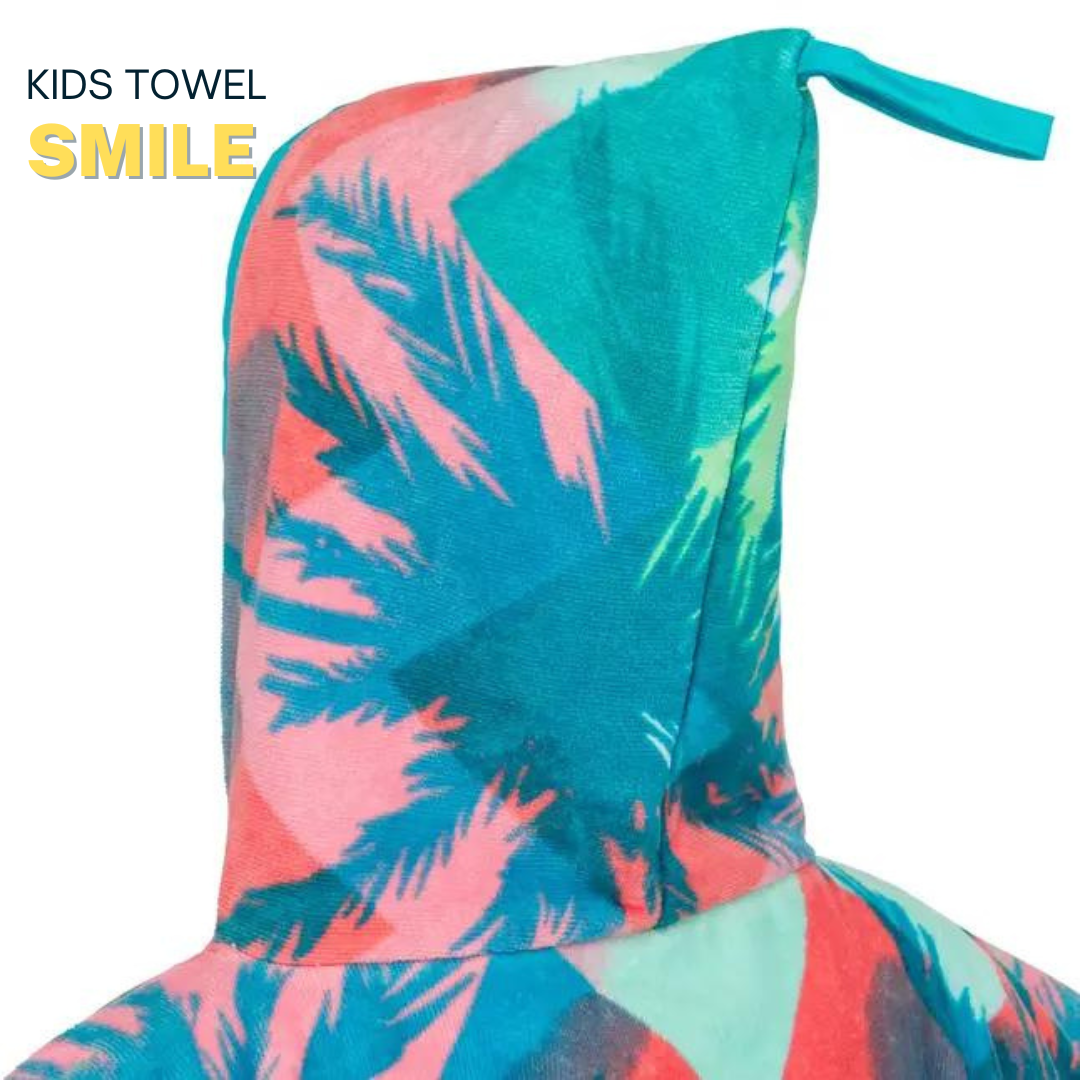 Child wearing a colorful hooded towel with palm tree and sailboat design, standing on a white platform.