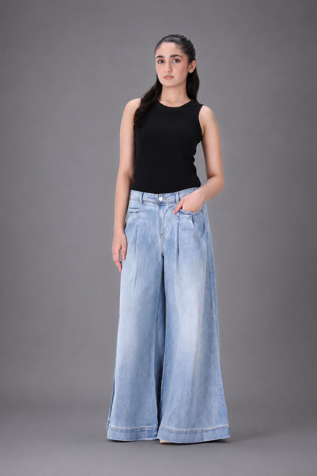 Woman wearing a black sleeveless top and light blue wide-leg jeans against a gray background