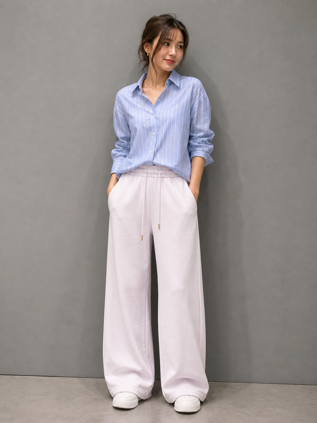 Woman wearing a light blue striped shirt and white pants against a gray background