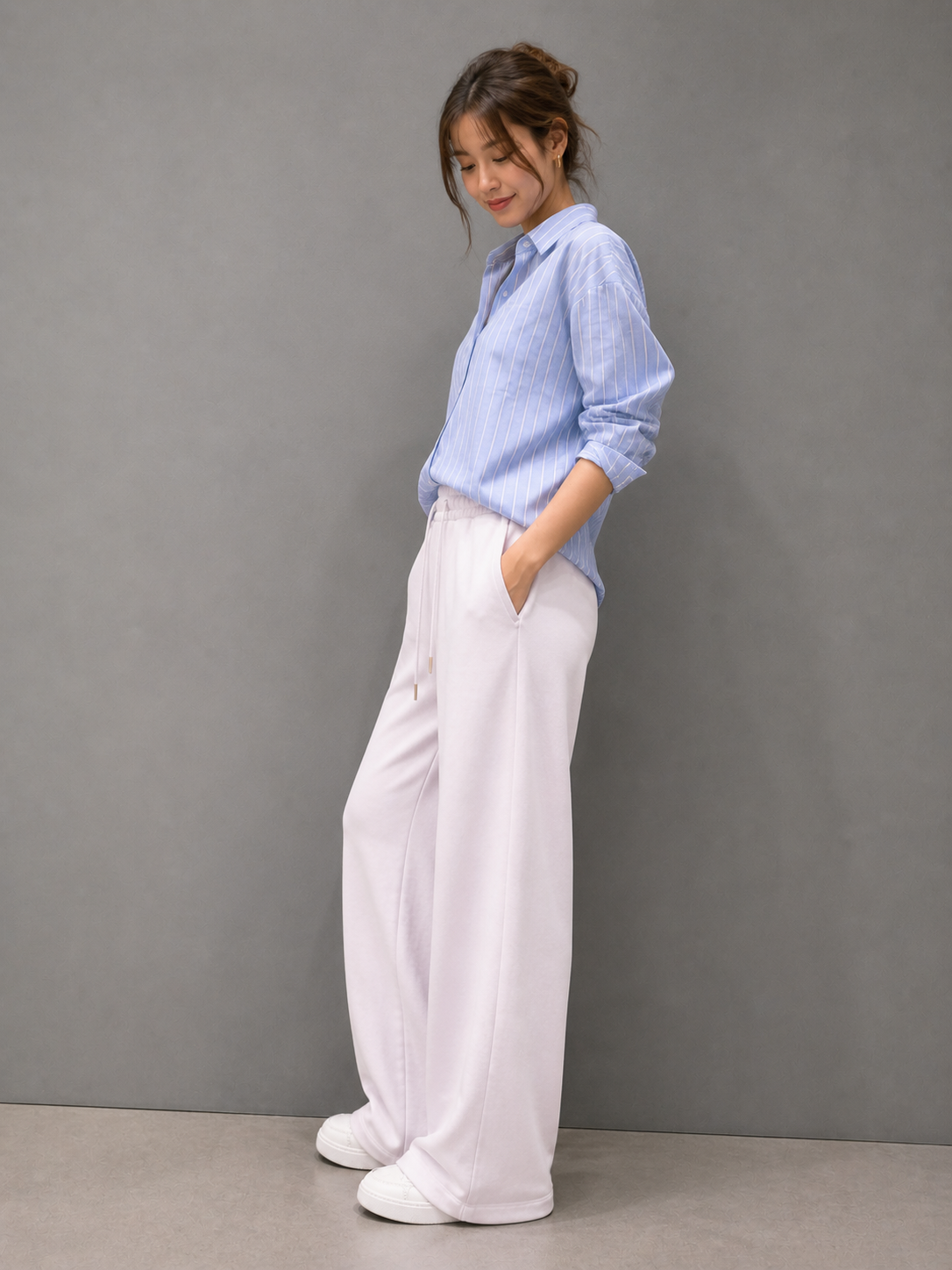 Person wearing a light blue shirt and white pants against a gray background