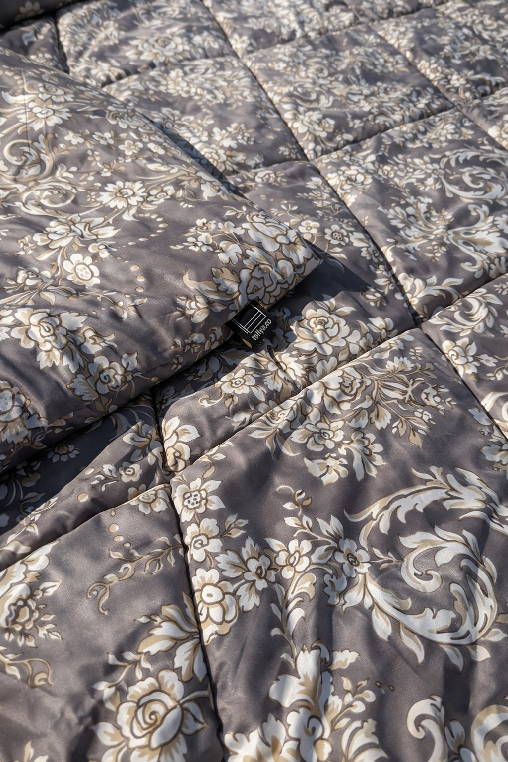 Close-up of a floral-patterned quilt with a brand label.