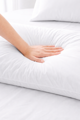 Hand touching a white pillow on a bed