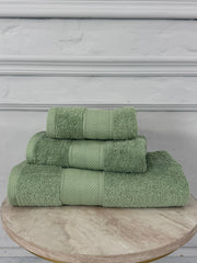 Set of three green towels stacked on a wooden surface with a gray wall background