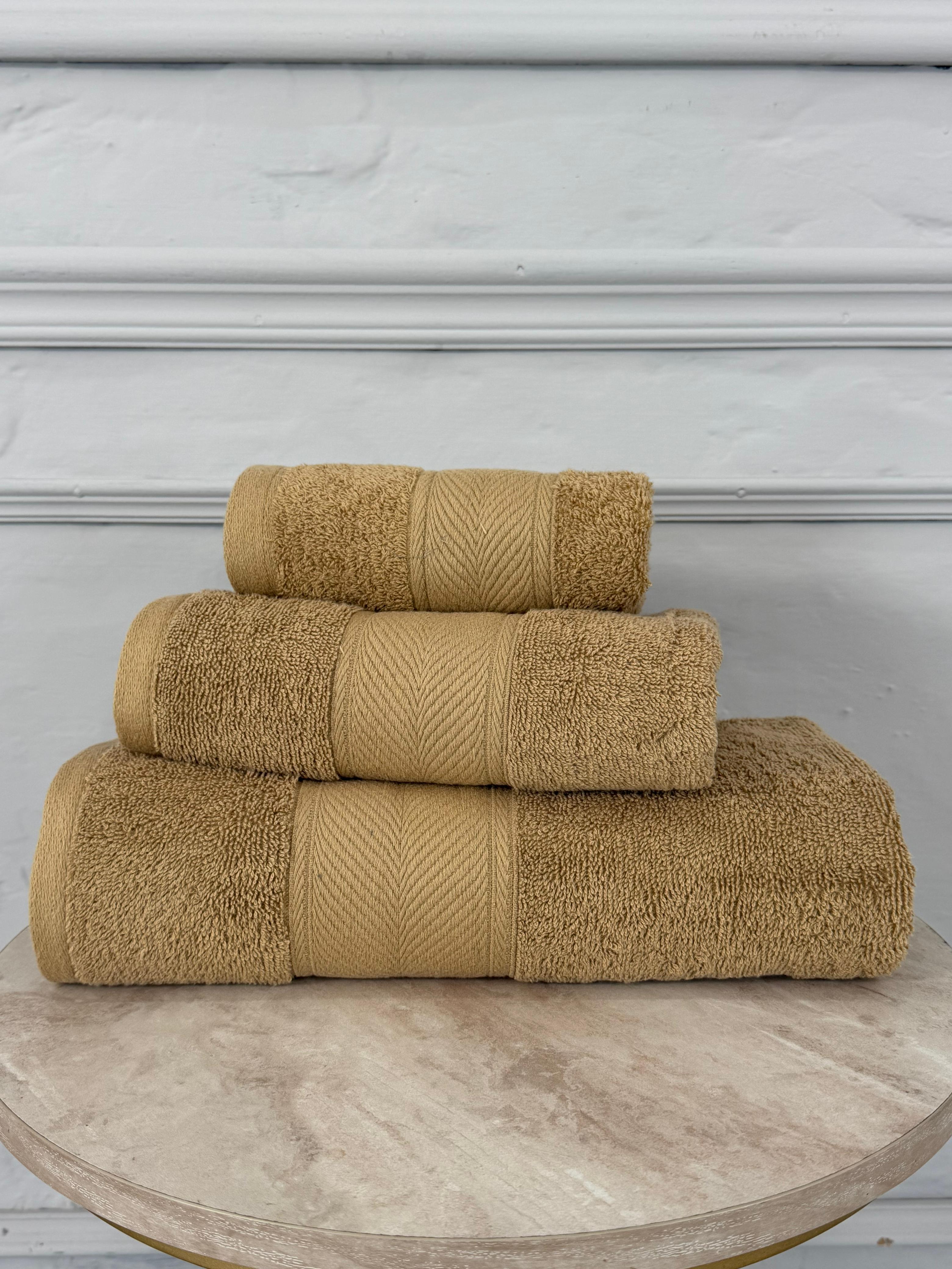 Three beige towels stacked on a wooden surface with a gray wall background