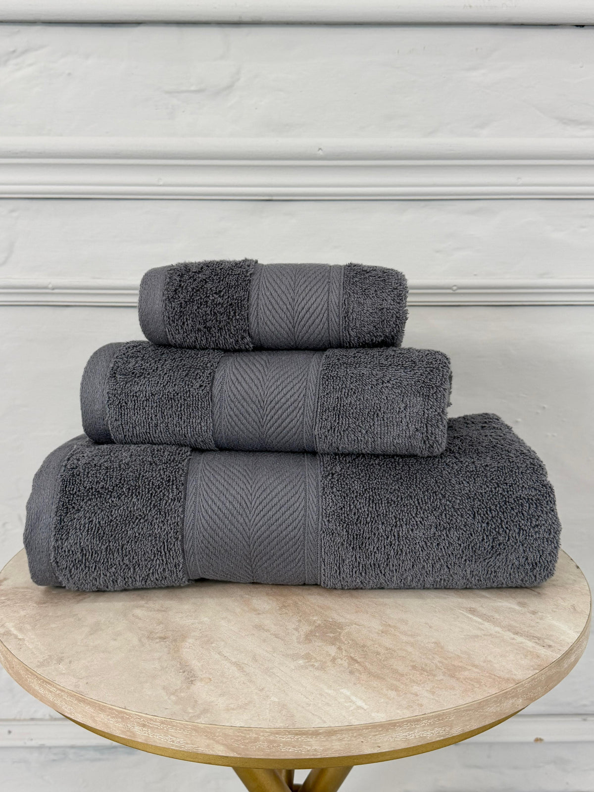 Stack of gray towels on a wooden table with a white wall background