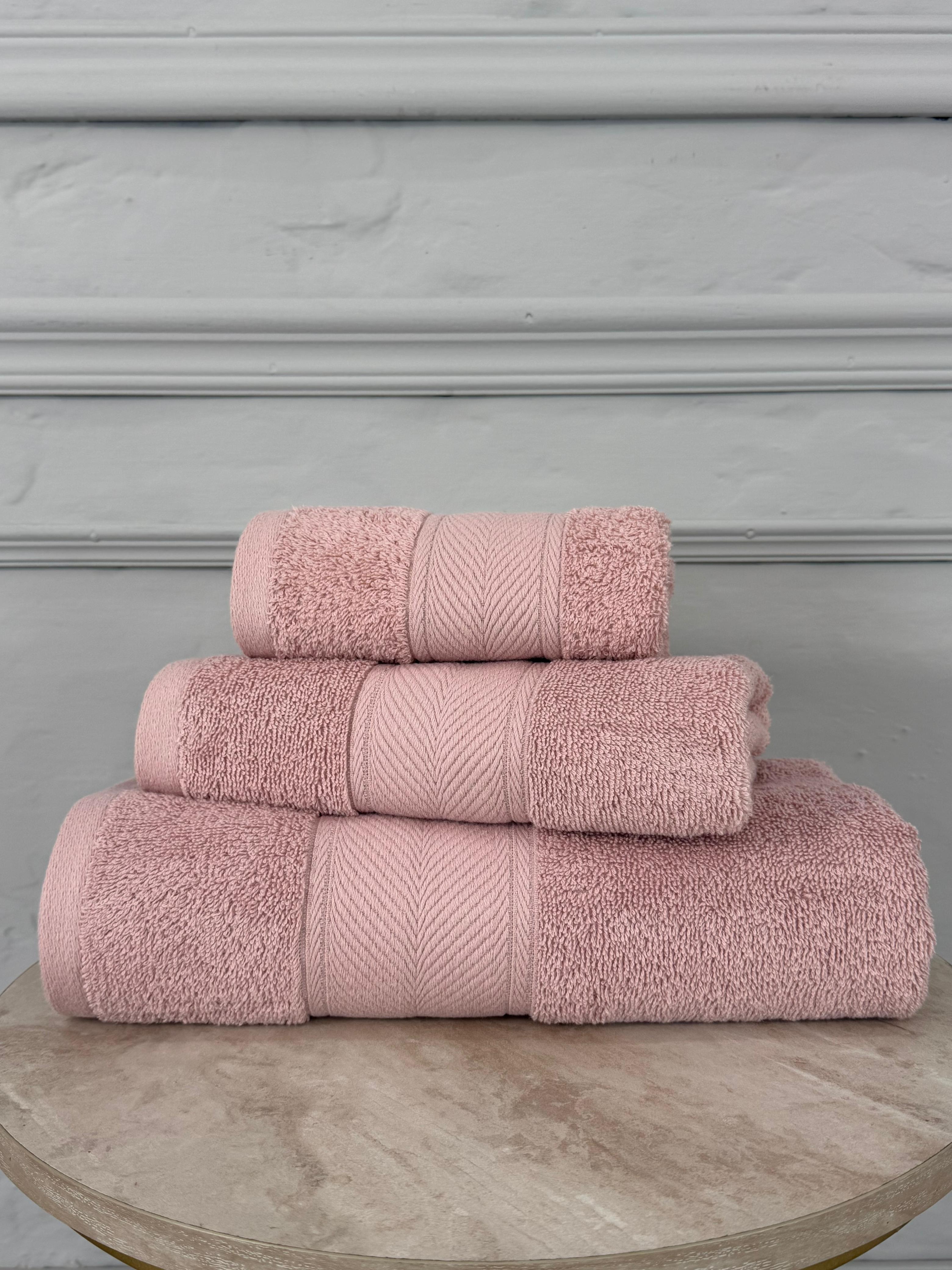 Set of three pink towels on a wooden surface with a gray background