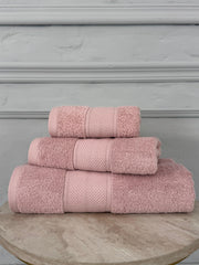 Set of three pink towels on a wooden surface with a gray background