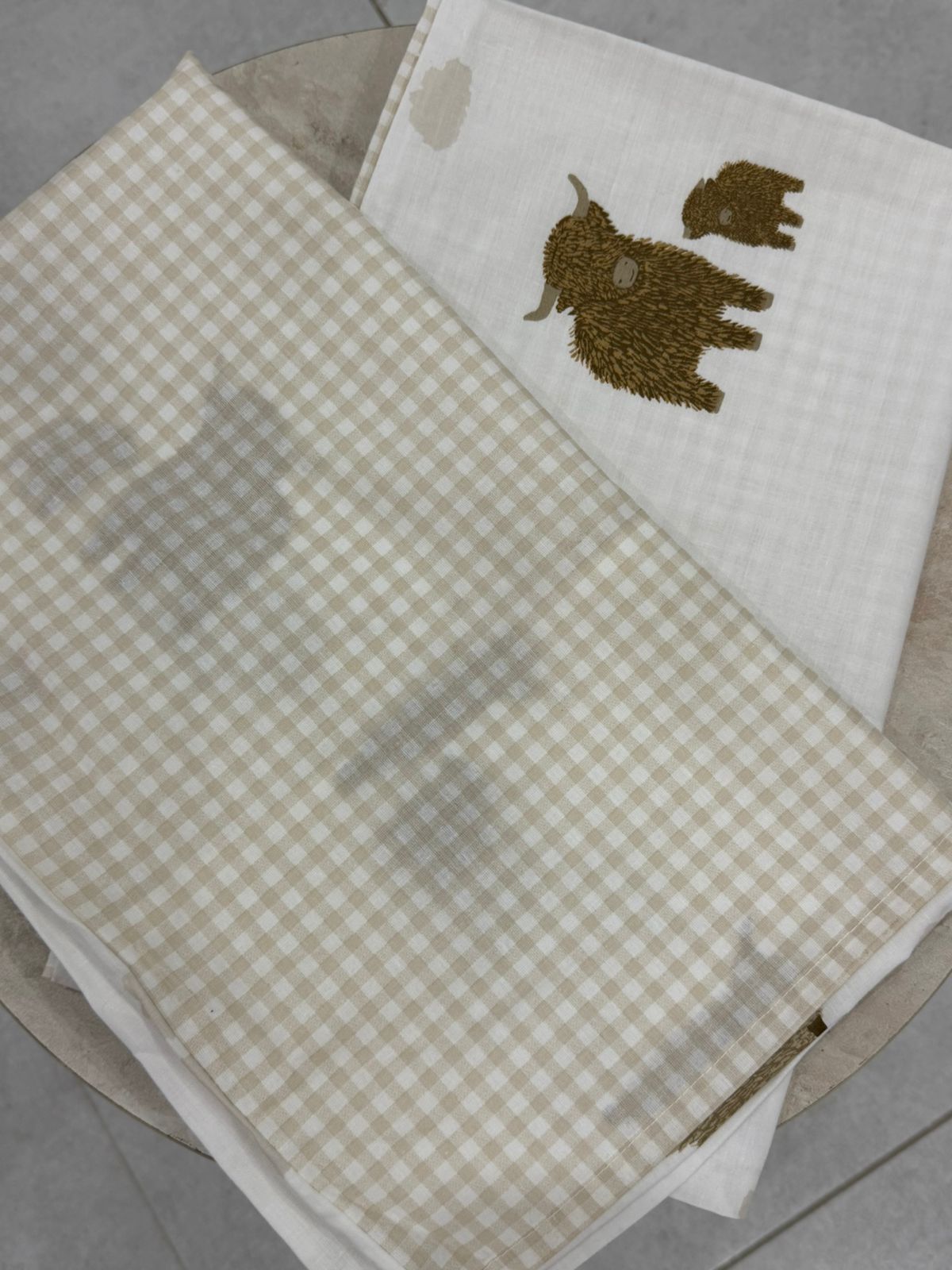 Two fabric swatches, one checkered and one with a embroidered design, on a gray surface.