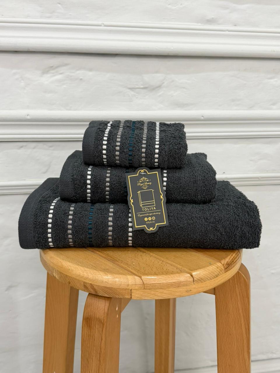 Set of black towels with a label on a wooden stool against a white wall.