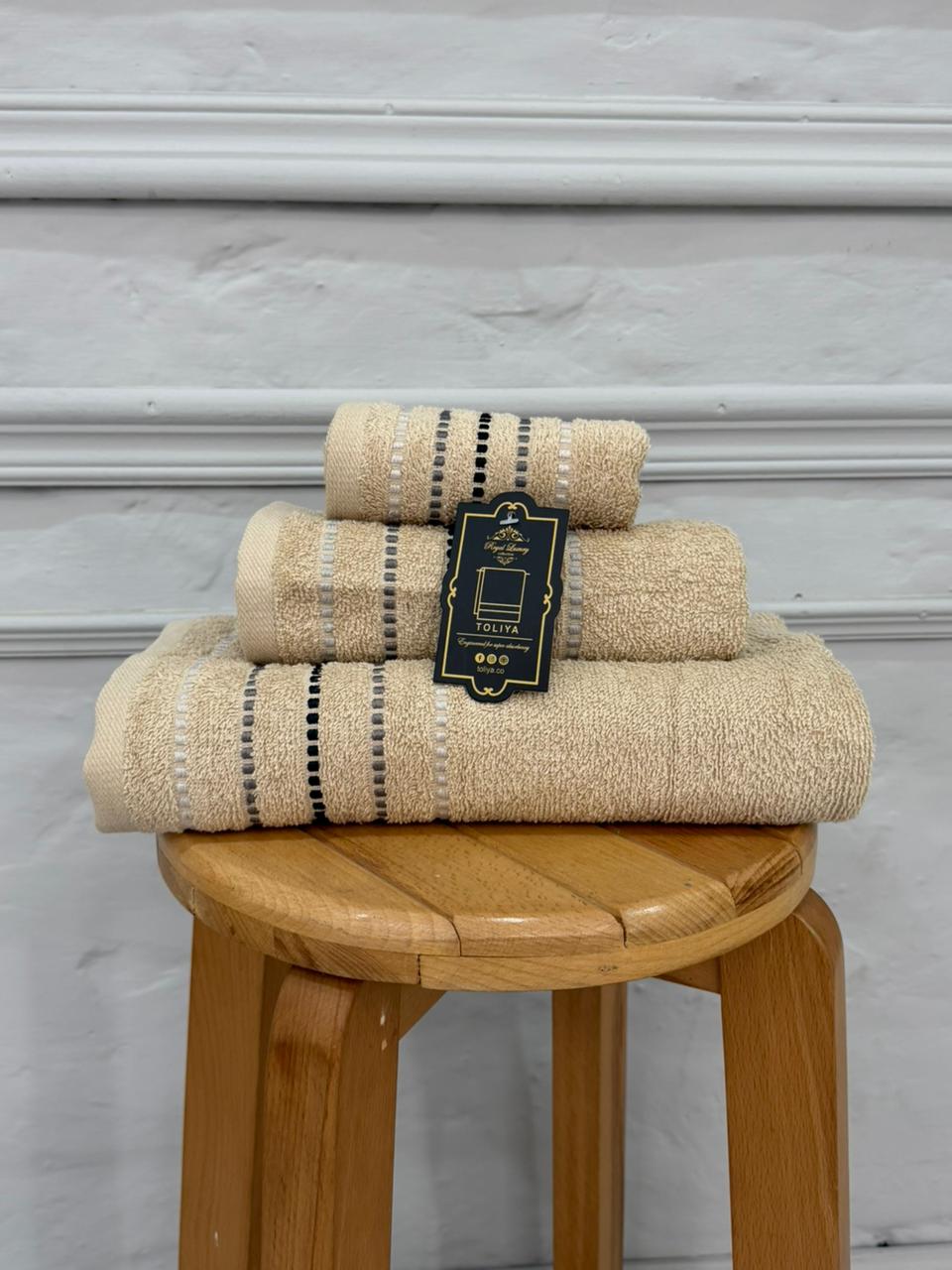 Set of beige towels with a tag on a wooden stool against a gray wall.