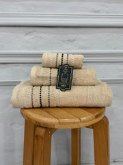 Set of beige towels with a tag on a wooden stool against a gray wall.