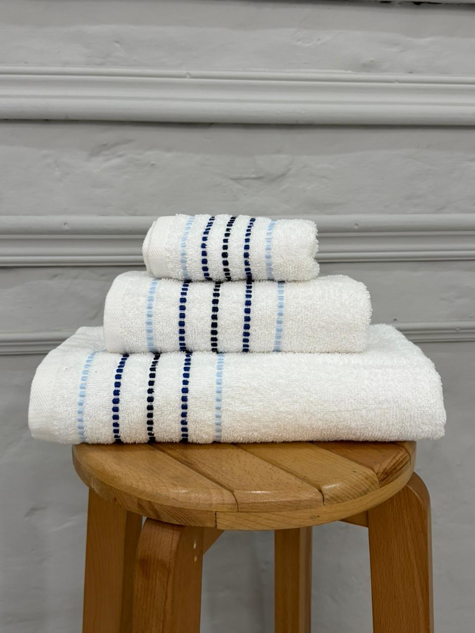 Stack of white towels with blue stripes on a wooden stool against a gray background