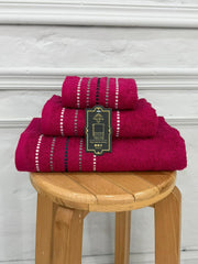 Set of three magenta towels with white stripes on a wooden stool against a white wall.