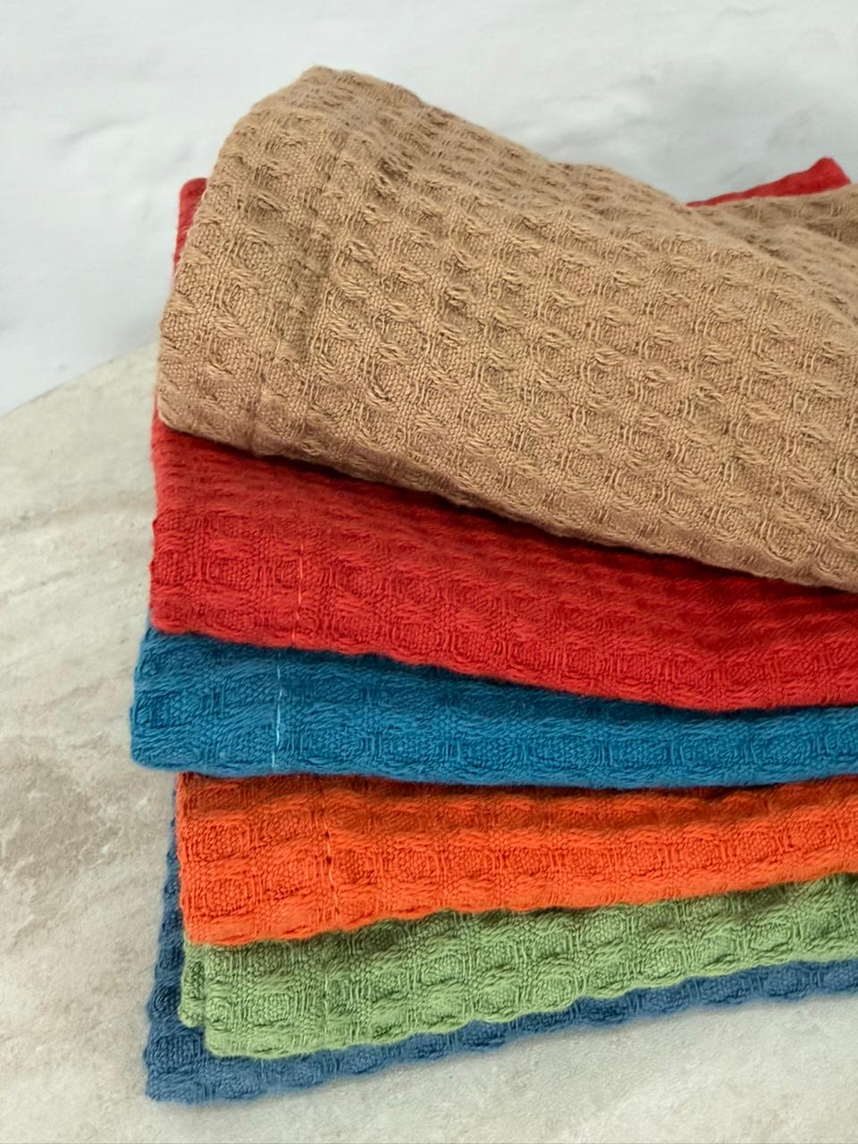 Stack of folded textured towels in various colors on a light background