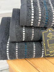 Stack of gray towels with decorative stripes and a brand tag on a wooden surface.