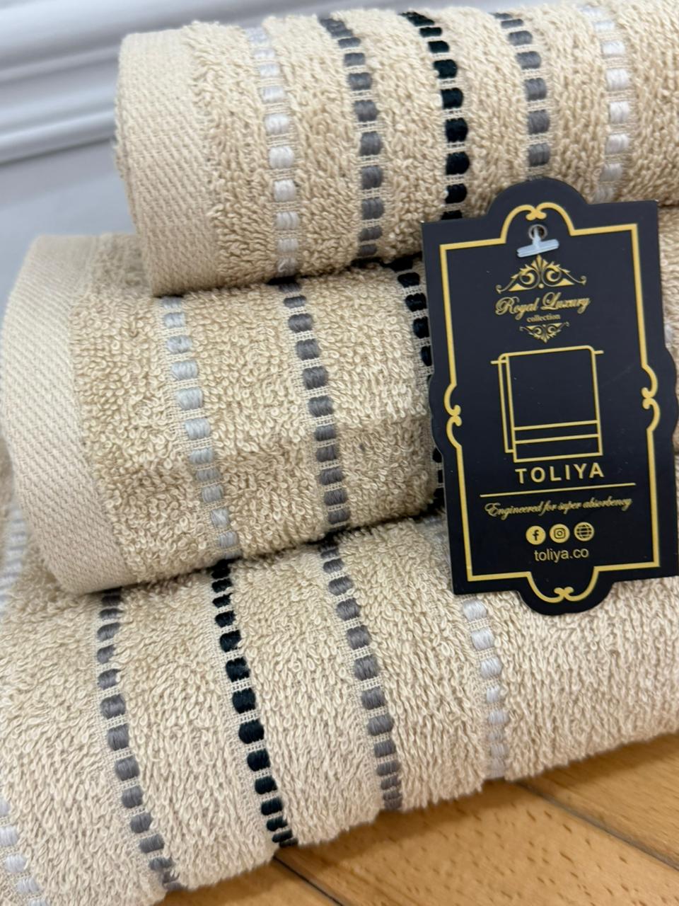 Three beige towels with black and gray stripes and a visible brand tag on a wooden surface.