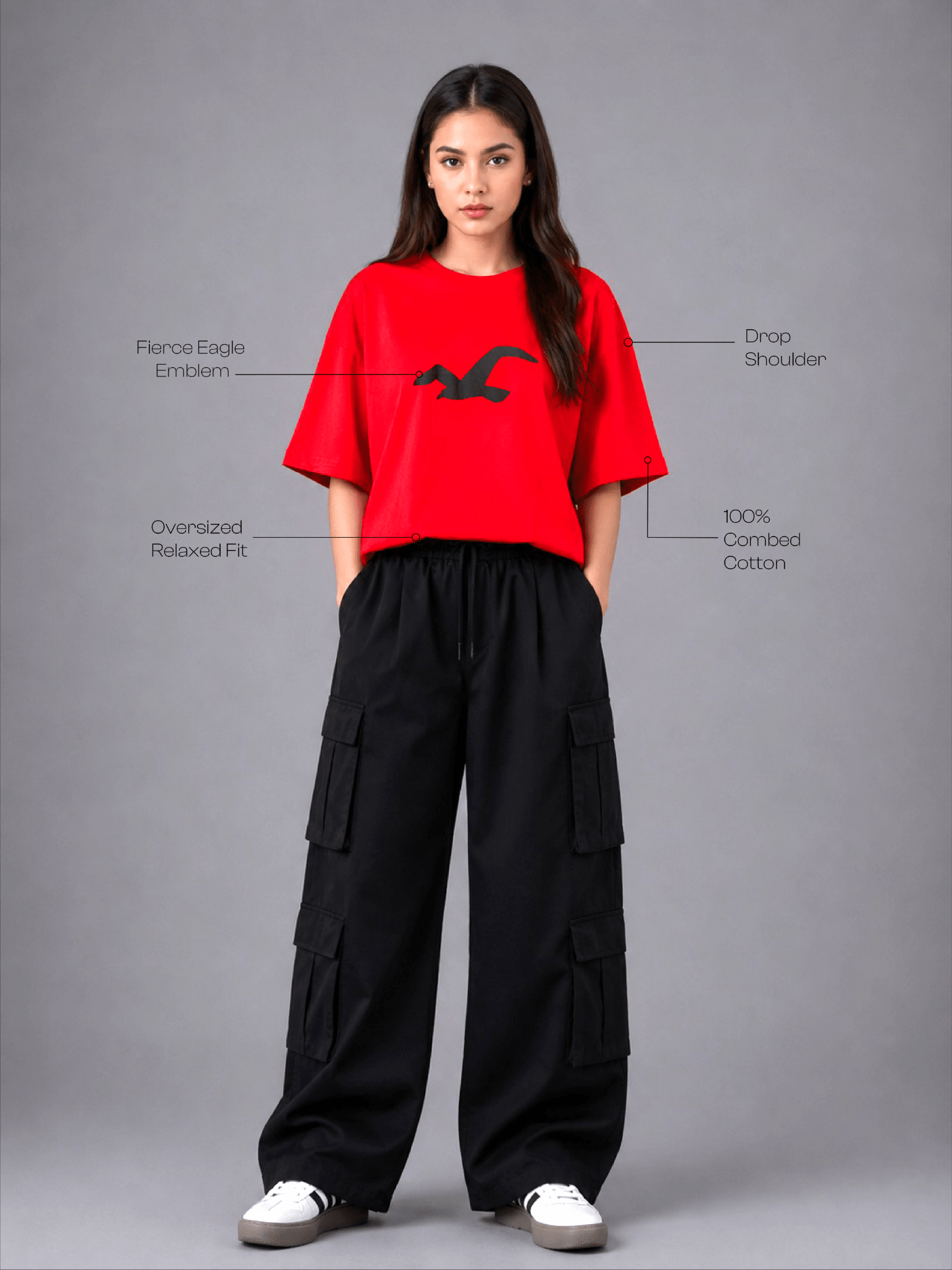 A model stands against a gray studio background wearing a bright red short-sleeve T-shirt with a black eagle emblem and black wide-leg cargo pants. White text callouts point to features of the shirt, including a 'Fierce Eagle Emblem,' 'Drop Shoulder,' 'Oversized Relaxed Fit,' and '100% Comfort Cotton.